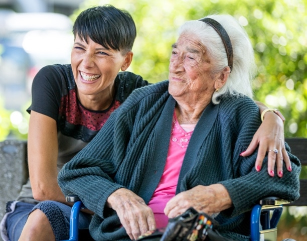 Caregiver and elderly woman in a wheelchair smiling at the park