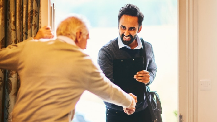 Caregiver shaking hands with a senior man while entering his house