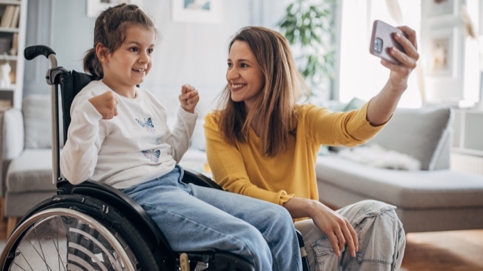 Mother and young kid who is in wheelchair enjoying together in living room at home.