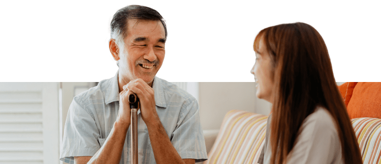 Female caregiver and man with a cane chatting in the living room