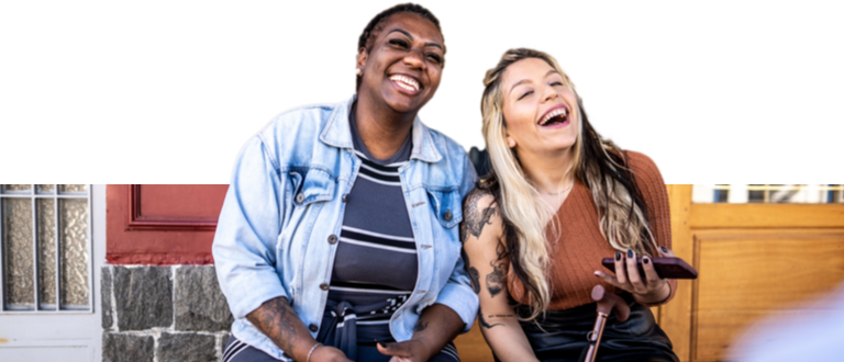 Young woman with a prosthetic leg smiling with another young woman on the porch of her home